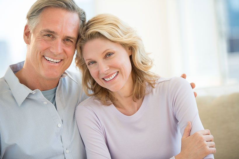 happy couple smiling with man's hand on her shoulder sitting on the couch