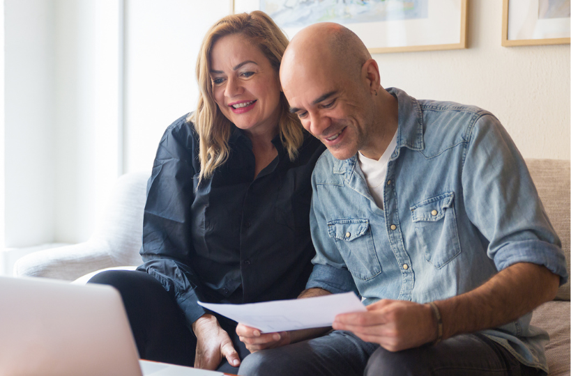 man and woman sitting on couch in living room looking at financial statement