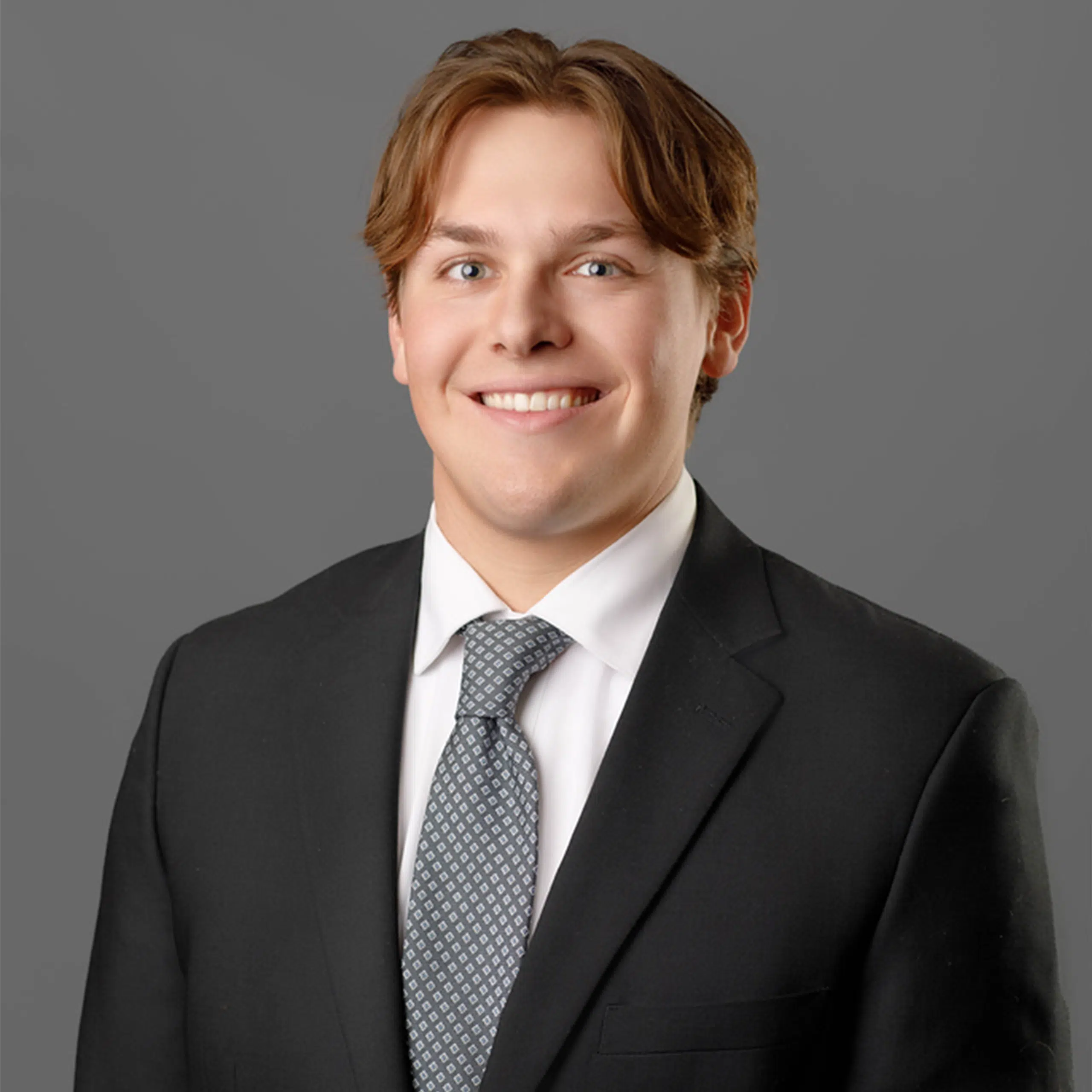 Billy Peterson smiling in a suit with a grey background