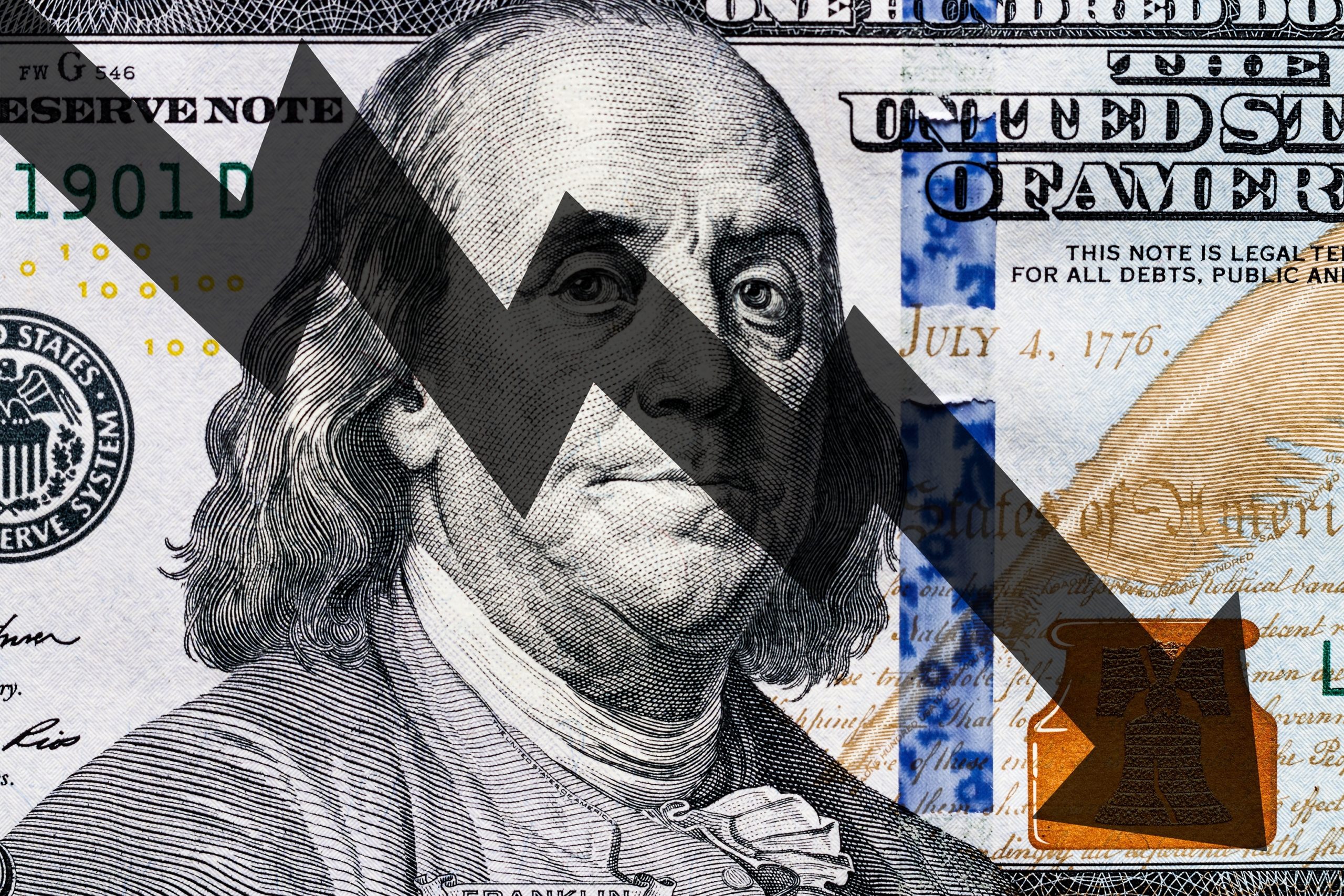 hundred dollar bill zoomed in to benjamin franklins face with a line chart pointing down to the bottom right corner